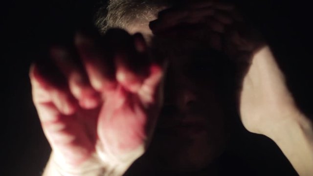 Scared young man knocking on the window glass bloody hand deep dark background