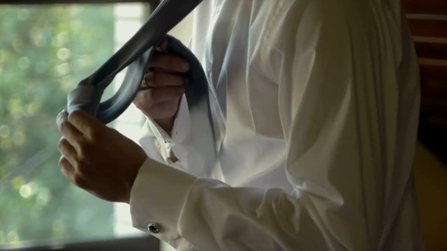 Man in white shirt tying a tie near the window