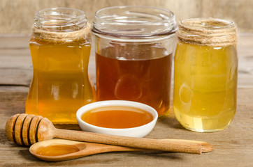 three jars,the bowl, the spoon with a honey on wooden background