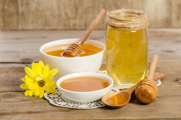 Yellow flower, jar, bowl and spoon with honey on wooden backgrou
