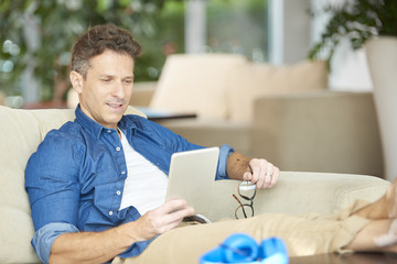 Shot of a smiling confident man using his tablet while relaxing on the sofa at home.