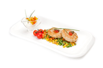 The dietary fish cutlets served on a white dish with a garnish from corn and asparagus haricot, with sauce, decorated by red caviar, isolated on a white background.