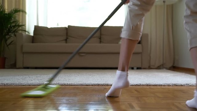Housewife dancing with a mop in the living room. Close-up of her legs. Dolly shot. Slow motion.