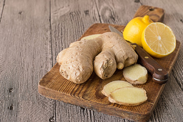  Lemon, ginger root and a knife on a cutting board on a gray wooden table.