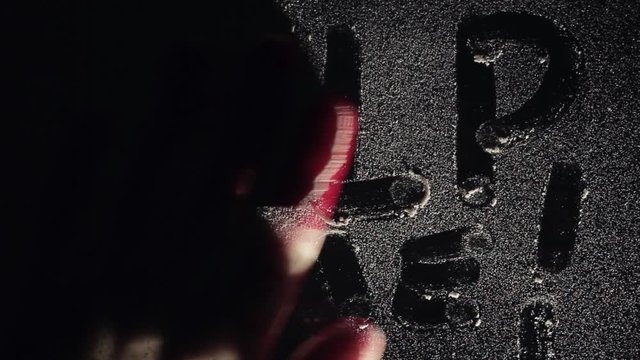 Bloody hand erasing inscription HELP from surface of dirty glass dark background