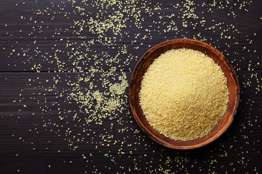 Raw couscous in bowl on dark wooden background from above