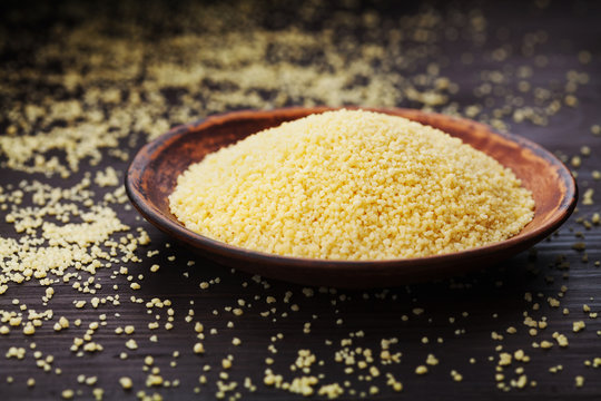 Raw couscous in bowl on dark wooden background