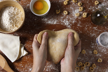 Female hands kneading dough on wooden table with ingredients. Top view. Rustic style
