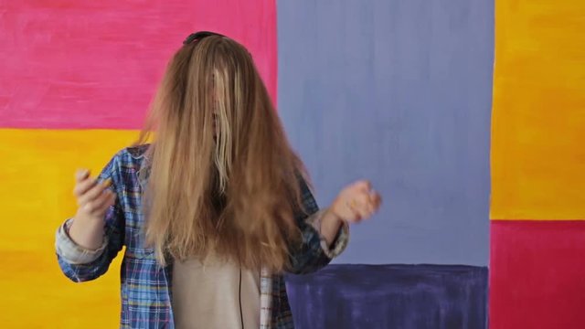 Woman listening to music, dancing and closing face by long hair. Colorful background