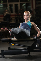 Woman doing strength exercises for abdominal muscles at indoor sport gym. Girl doing yoga stretches after running. Fitness model in dark sport club. 