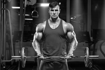 Muscular man working out in gym doing exercises with barbell at biceps