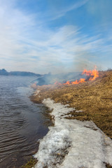 Burning dry grass on the river bank. Spring. Snow and fire.