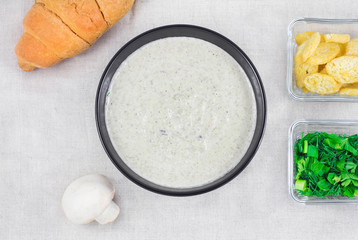 Mushroom cream soup with greenary on the table with croissant, rosemary, cracker and mushroom. Delicious fresh soup for lunch.