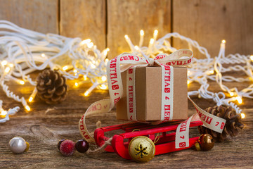 Handmade gift box on sledge with christmas lights on wooden background
