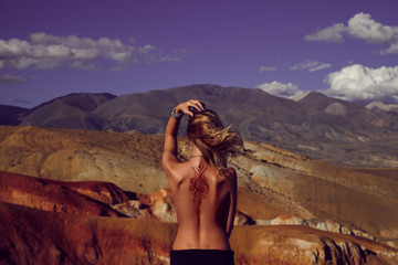 Woman with mehendi on back sitting in colorful mountains backgro