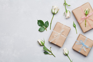 Gift or present box wrapped in kraft paper and rose flower on gray table from above. Flat lay styling. Copy space for text.