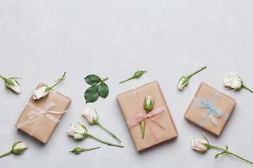 Gift or present box wrapped in kraft paper and rose flower on gray table top view. Flat lay styling. Copy space for text.