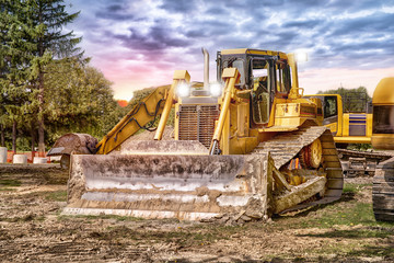 Large bulldozer at construction site, sunset in background.