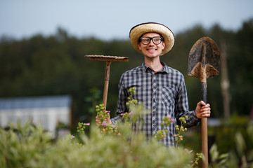 Funny gardener holding a shovel and rake outdoors