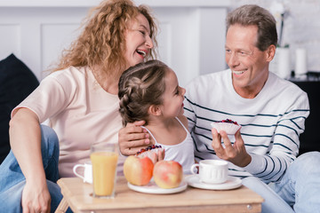 Laughing girl holding berry cupcakes with her grandparents