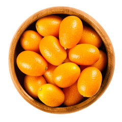 Fresh kumquats in a wooden bowl on white background, also called cumquats and Nagami kumquat. Edible small oval orange fruits of Fortunella margarita. Isolated macro food photo close up from above.