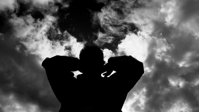 Dark and mysterious silhouetted figure lifts hood over head and disappears, black and white treated.