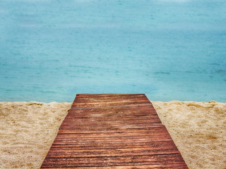 Wooden path on sand beach, sea in the background.