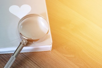 Magnifier over the book on wooden table with light flare and copy space