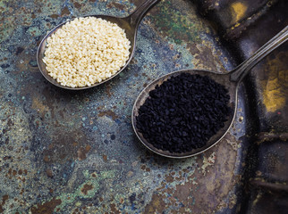 White and black sesame seeds in metal spoons on vintage background

