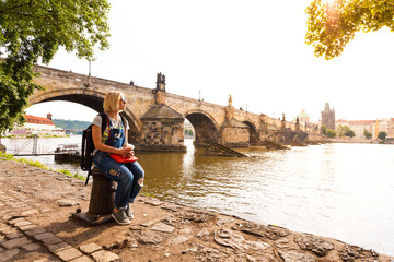 Female traveler enjoys views of the Charles Bridge in Prague. Czech Republic. Charles Bridge with its statuette, Old Town Bridge Tower, St. Francis Of Assissi Church in the background.