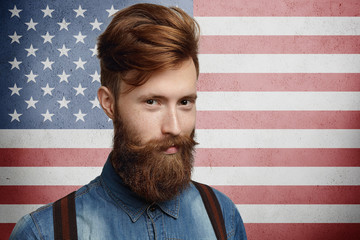 National identity and citizenship concept. Studio shot of good-looking unshaven Caucasian macho dressed in trendy clothes, looking at camera with attractive smile posing on American flag background