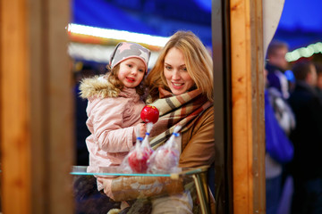 Mother and little kid girl eating crystalized apple on Christmas
