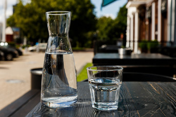 A glass of water and a water-bottle on a black wooden table of a city cafe terrace