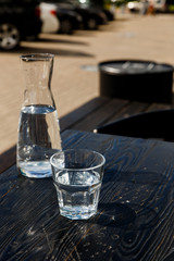 A glass of water and a water-bottle on a black wooden table of a city cafe terrace