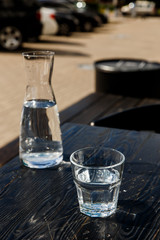 A glass of water and a water-bottle on a black wooden table of a city cafe terrace