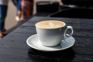 A white cup of cappuccino on the dark wooden table