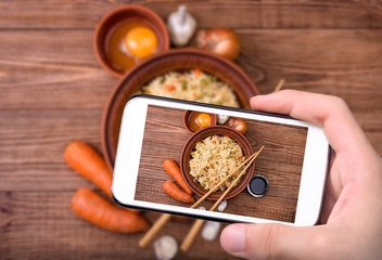 Hands taking photo fried rice with vegetables  and eggs with smartphone.