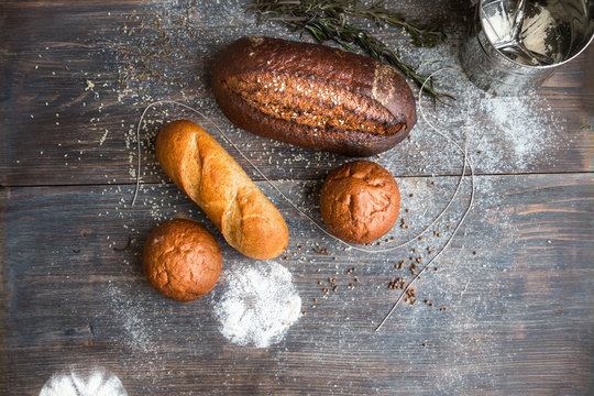 Different breads - rye, dark, roll, French baguette - on wooden table dusted with flour. Copy space. Top view.