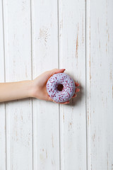 Female hand holding sweet donut on wall paneling background