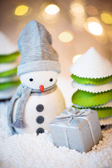 Cute festive snowman with Christmas present, Christmas lights in background