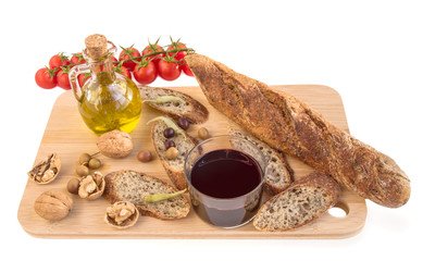 Tray with baguette, nuts, olives, oil, vine, tomatoes on white.