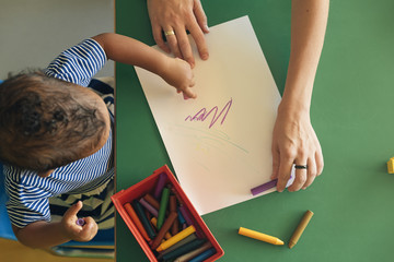 Little child and mother are drawing on a paper.