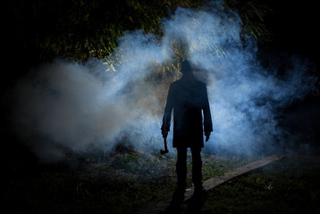 spooky man wih axe in the dark smoke filled forest - obrazy, fototapety, plakaty