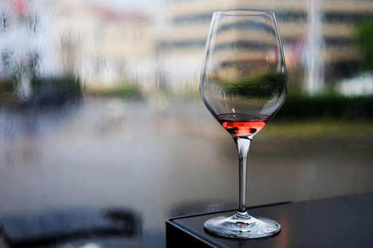 A dark image of a wine glass with a bit of rose wine and drops on the glass. Selective focus. Small depth of field.