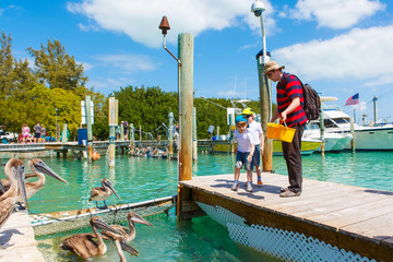 father and two little kid boys feeding fishes and pelicans