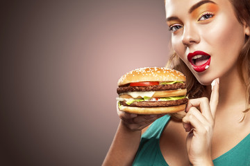 Closeup portrait. Beautiful blond young woman having fun eating big burger. Advertisment for cafe.