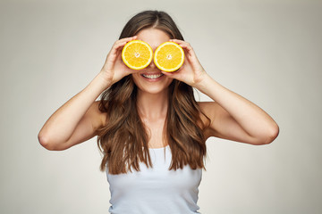 Smiling woman holding two half og oranges fruit ahead of eyes.