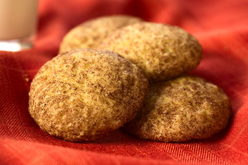 Snickerdoodle cookies with cinnamon and sugar coating on red fabric, photographed with natural light (Selective Focus, Focus in the middle of the left cookie and the front edge of the right one)