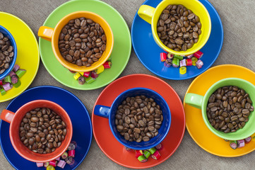 colorful cup and saucer filled with coffee beans and candy on the saucer. View from above. colorful candy on the saucer. Cups with coffee beans inside.