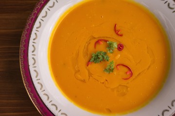 Creamy pumpkin or butternut soup asian style served in the rustical old deep plate. Main ingredients are butternut or Hokaido pumpkin, fresh hot pepper, carrots and chicken bouillon on wooden table. 